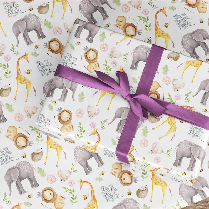 Pode incluir: Um presente embrulhado em papel branco com um padr&atilde;o repetitivo de ilustra&ccedil;&otilde;es em aguarela de elefantes, girafas, le&otilde;es e coelhos com folhagem verde e abelhas, atado com um la&ccedil;o largo de fita de cetim roxo escuro.