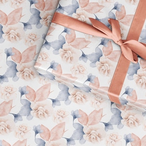 May include: A gift box wrapped in white paper with a delicate floral pattern in shades of pink and blue. The box is tied with a wide, peach-colored satin ribbon.