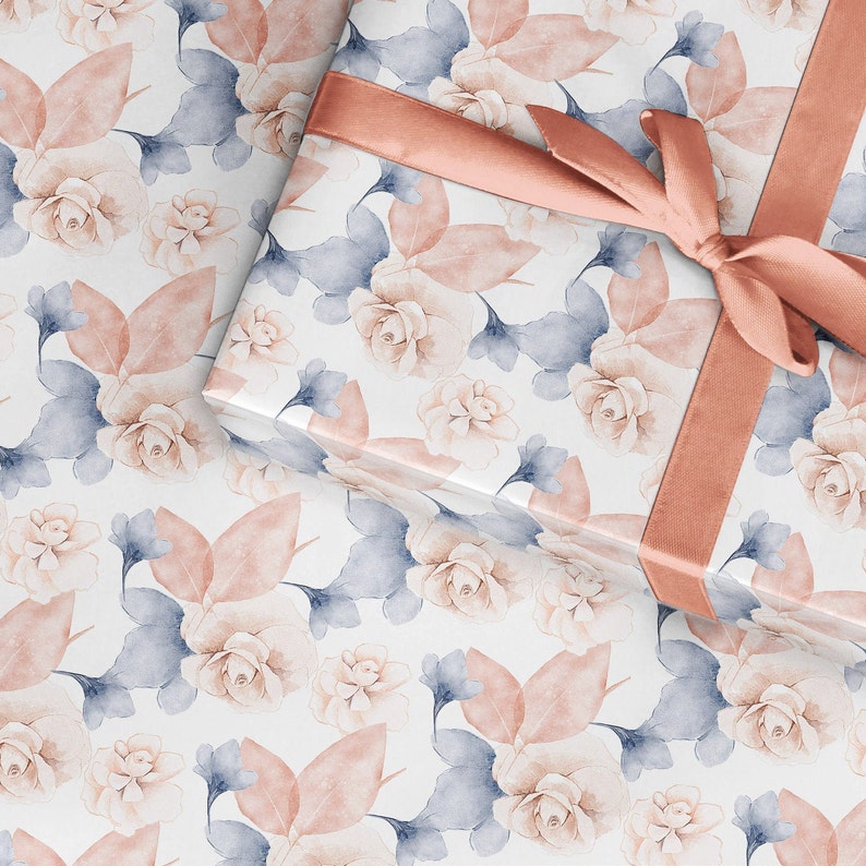 May include: A gift box wrapped in white paper with a delicate floral pattern in shades of pink and blue. The box is tied with a wide, peach-colored satin ribbon.