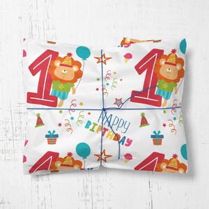 May include: White wrapping paper with a repeating pattern of colorful confetti, stars, and a lion wearing a party hat. The number "1" is in red with the words "Happy Birthday" in a colorful font.