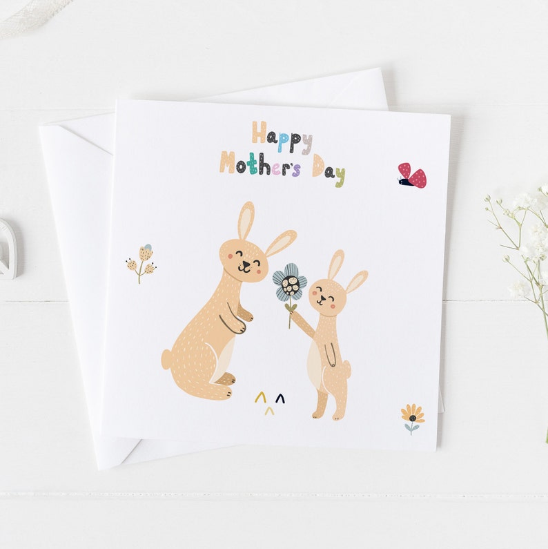 May include: A card with a colorful "Happy Mother's Day" message and two brown bunnies. One bunny is holding a blue flower and the other is smiling. There is a red butterfly in the top right corner.