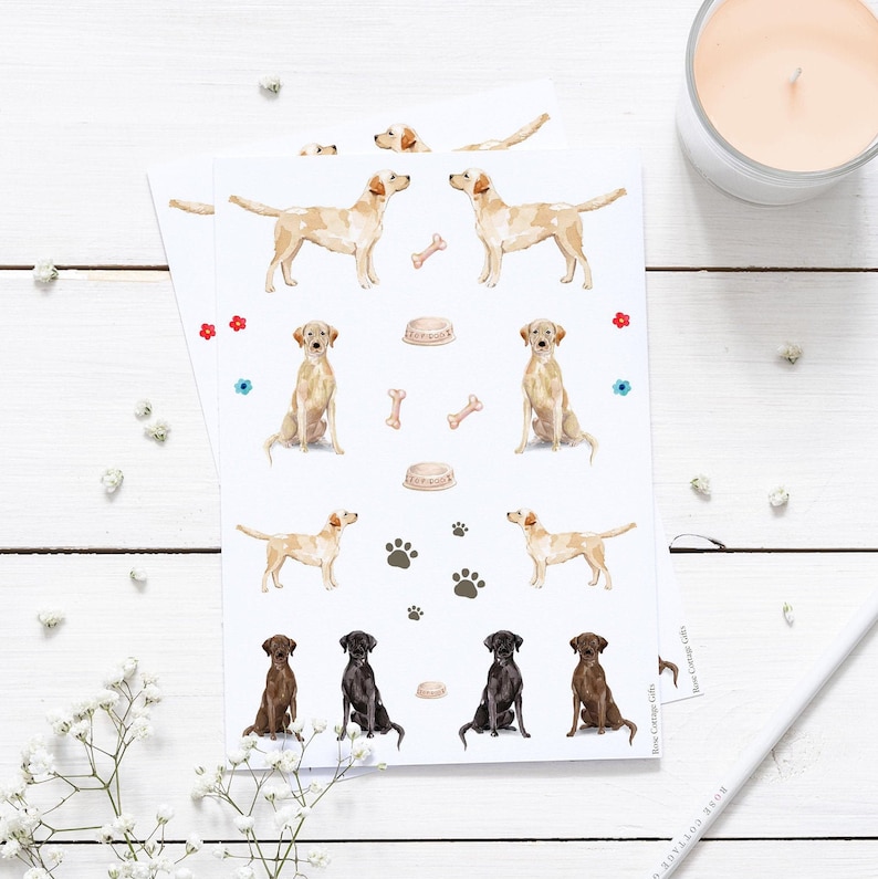 May include: A sheet of stickers featuring watercolor illustrations of Labrador Retrievers in various poses. The stickers include images of dogs sitting, standing, and playing with a bone and a bowl. There are also paw prints and small flowers on the sheet.