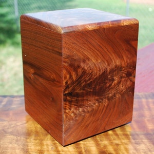 May include: A square wooden box with a rich brown wood grain. The box is made of solid wood and has a smooth finish.