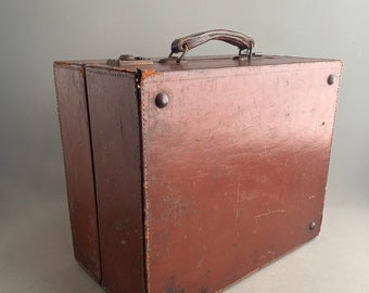 May include: A vintage brown leather suitcase with a metal handle and brass accents. The suitcase has a worn and distressed look, suggesting it has been well-traveled.