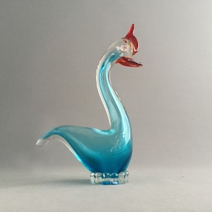 Op de afbeelding: Een blauwe glazen zwanenfiguur met een rood en wit hoofd en een heldere glazen voet.