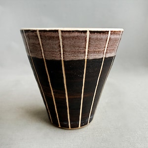 Könnte beinhalten: Handgefertigte Keramikschale mit einzigartigem Design. Die Schale hat einen dunkelbraunen Boden mit vertikalen cremefarbenen Streifen. Der obere Teil ist hellbraun, und der Rand ist weiß.