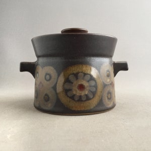 May include: A brown ceramic casserole dish with a lid and two handles. The dish features a floral pattern in shades of brown, yellow, white, and red.