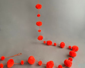 May include: A long garland of bright orange pom-poms strung together with twine. The garland is perfect for adding a festive touch to any room.