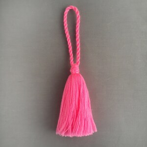 Può includere: Un fiocco rosa acceso con un anello annodato in cima. Il fiocco è fatto di filato morbido e soffice.