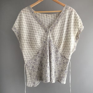 May include: A white and purple floral print top with a V-neck and short sleeves. The top has a tie at the side.