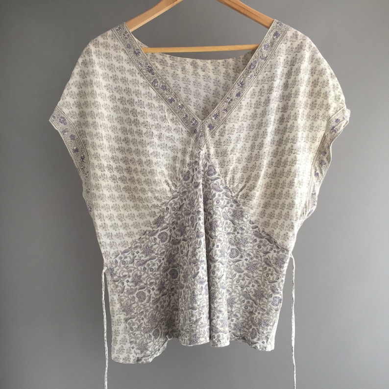 May include: A white and purple floral print top with a V-neck and short sleeves. The top has a tie at the side.