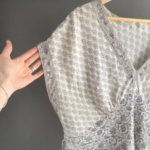 May include: A white and purple floral print kaftan with a V-neckline and short sleeves. The kaftan is made of a lightweight fabric and has a relaxed fit.