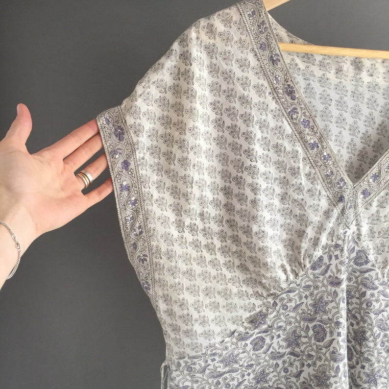 May include: A white and purple floral print kaftan with a V-neckline and short sleeves. The kaftan is made of a lightweight fabric and has a relaxed fit.