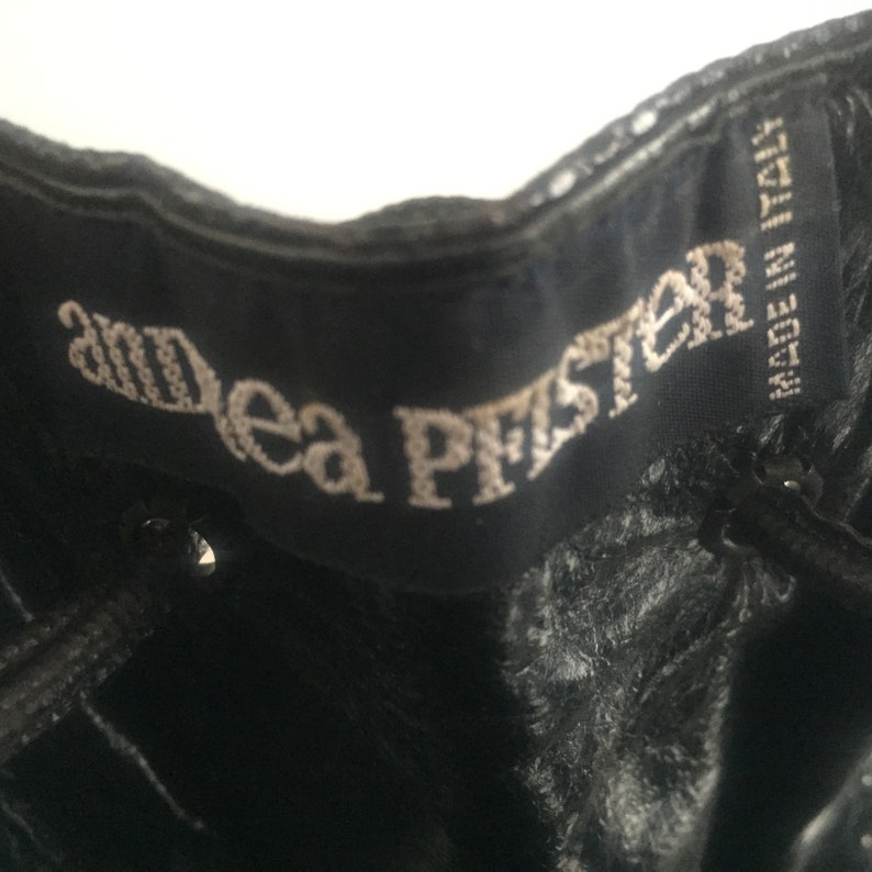 May include: Close-up of a black leather boot with a white embroidered label that reads "Andrea Pfister" and the text "Made in Italy".