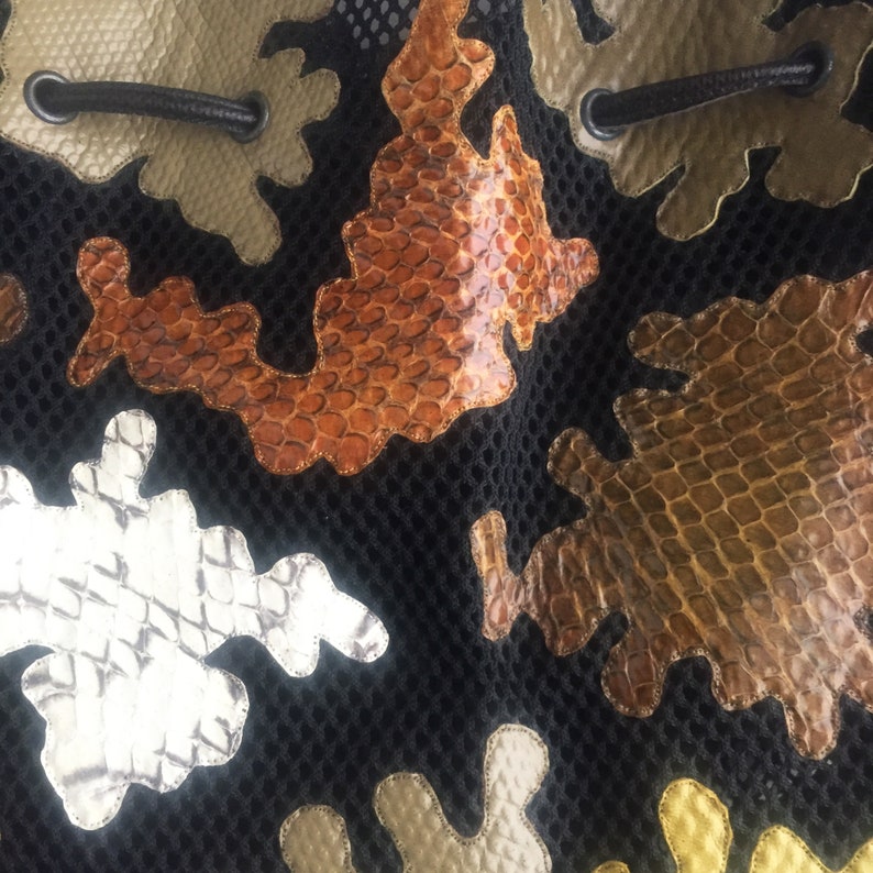 May include: A black mesh bag with different colored snakeskin patches. The patches are in various shapes and sizes, including brown, orange, silver, and gold.