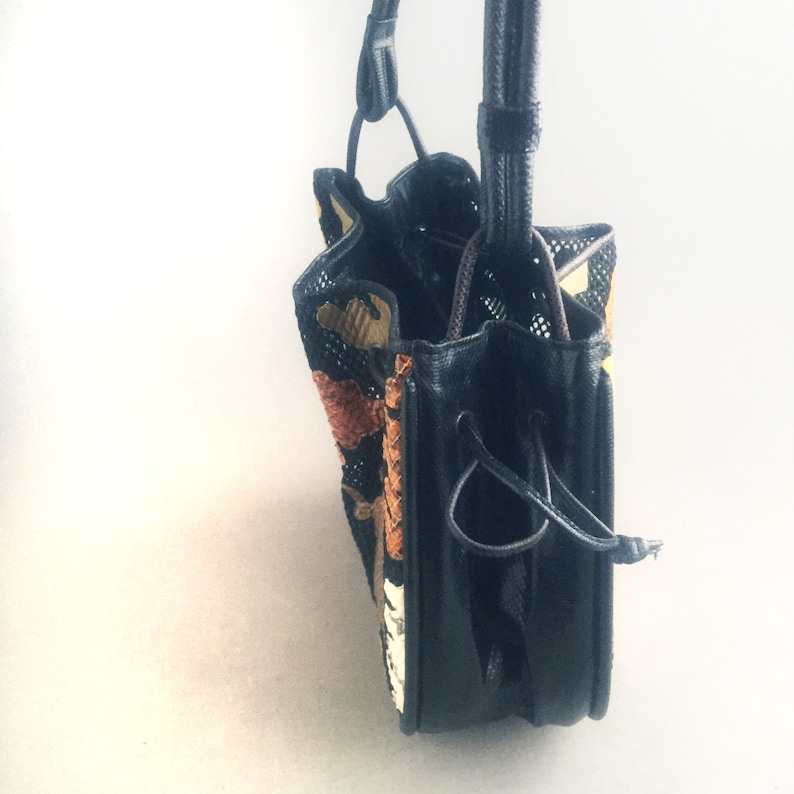 May include: A black and brown patterned drawstring bag with a black leather bottom. The bag has a long black strap.