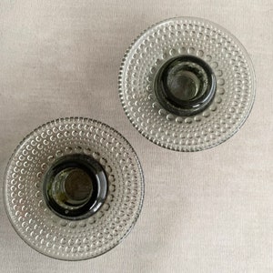May include: Two clear glass candle holders with a textured, bubble-like design. The holders are a light grey colour.