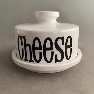 Può includere: Ciotola per formaggio in ceramica bianca con un'etichetta "Formaggio" nera. La ciotola ha un coperchio e una base.
