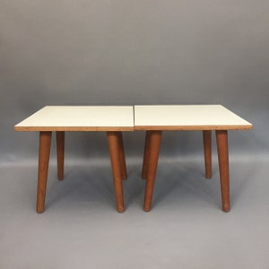 May include: Two white square tables with wooden legs. The tables are side by side and are made of a light wood.