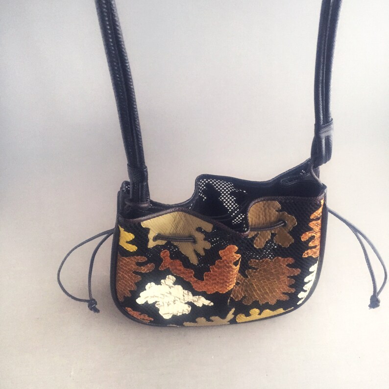 May include: A black leather bucket bag with a drawstring closure. The bag is decorated with a colorful geometric pattern in shades of brown, gold, and white.