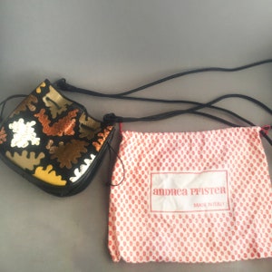 May include: A black bucket bag with a colorful geometric pattern and a drawstring closure. The bag comes with a dust bag that has the text "andrea pfister made in italy" printed on it.