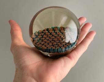 Puede incluir: Un pisapapeles de vidrio transparente con un patrón de vidrio naranja y turquesa en espiral en su interior.