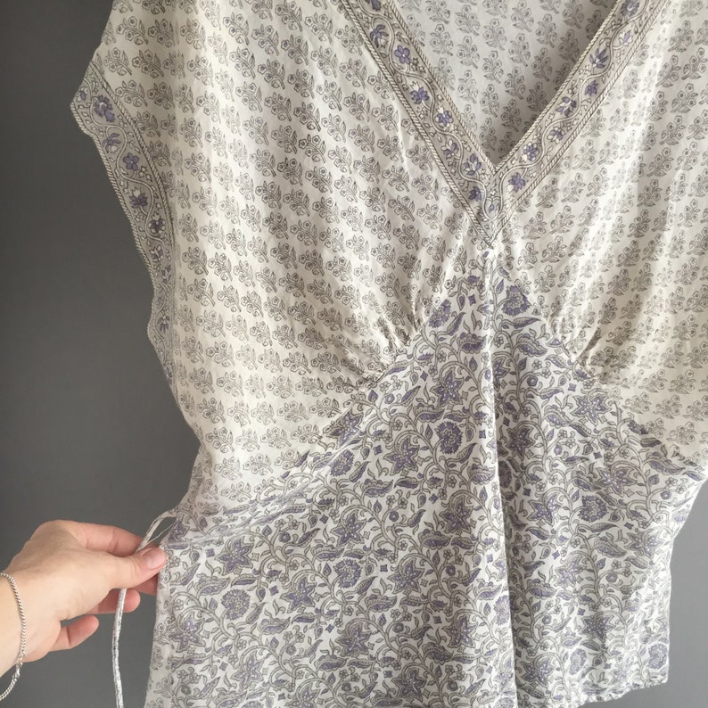 May include: A white and purple floral print top with a V-neck and a gathered detail at the waist.