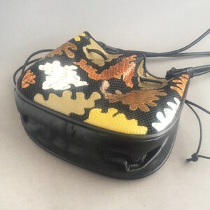 May include: A black leather drawstring bag with a colorful geometric pattern. The pattern features brown, yellow, and silver accents.