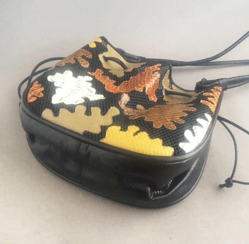 May include: A black leather drawstring bag with a colorful geometric pattern. The pattern features brown, yellow, and silver accents.