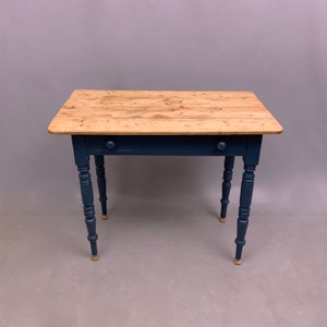 May include: A small wooden table with a single drawer painted in a dark blue colour. The table has turned legs and a light wood top.
