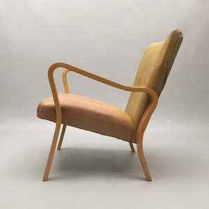 May include: A light brown armchair with a curved wooden frame and a light brown fabric seat and back.