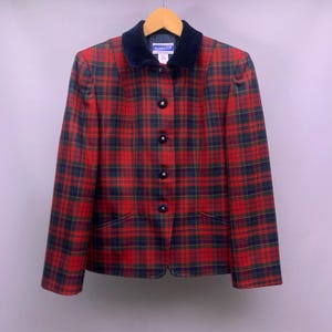 May include: A red, green, and navy plaid blazer with a navy velvet collar and gold buttons. The blazer is hanging on a wooden hanger. The blazer has two front pockets and a tailored fit. The Pendleton label is visible on the collar.