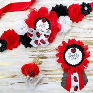 May include: Red, black, and white ladybug themed baby shower sash set with the text "Mommy to be" and "Daddy to be".