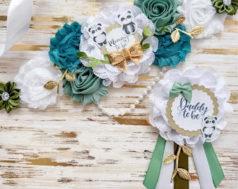 May include: A white and teal floral sash with panda bears and the text "Mommy to be" and a matching white and teal floral boutonniere with the text "Daddy to be" and a panda bear.