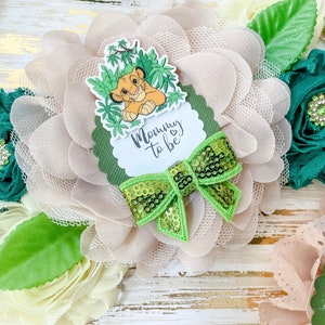 May include: A light brown and green floral headband with a green bow and a white circle with the text "Mommy to be" and a cartoon lion cub.