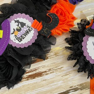 Puede incluir: Dos decoraciones para baby shower con tem&aacute;tica de Halloween. Una presenta un sombrero de bruja y el texto "A Baby is Brewing". La otra presenta un sombrero de bruja y el texto "Daddy to be".
