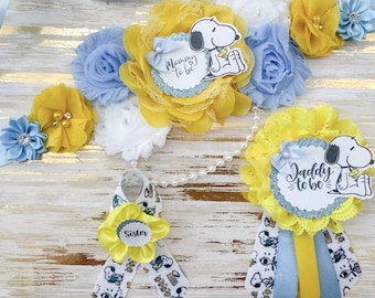 May include: A set of fabric badges featuring Snoopy and Woodstock. One badge has yellow and blue flowers with the text Mommy to be. Another badge has yellow flowers and ribbons with the text Daddy to be. A smaller badge features the text Sister.
