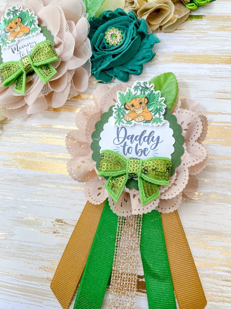 May include: A light brown and green flower with a green bow and a lion character in the centre. The flower has a scalloped edge and a white label that says "Daddy to be".