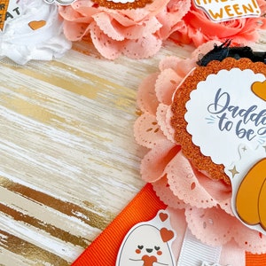 K&ouml;nnte beinhalten: Eine Sammlung von Babyparty-Dekorationen zum Thema Halloween. Die Dekorationen umfassen orangefarbene und wei&szlig;e B&auml;nder, Spitze und Abzeichen mit den Texten "Mommy to be" und "Daddy to be". Au&szlig;erdem gibt es Geister- und K&uuml;rbisaufkleber.