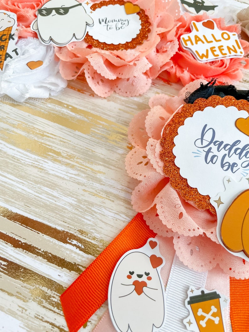 K&ouml;nnte beinhalten: Eine Sammlung von Babyparty-Dekorationen zum Thema Halloween. Die Dekorationen umfassen orangefarbene und wei&szlig;e B&auml;nder, Spitze und Abzeichen mit den Texten "Mommy to be" und "Daddy to be". Au&szlig;erdem gibt es Geister- und K&uuml;rbisaufkleber.