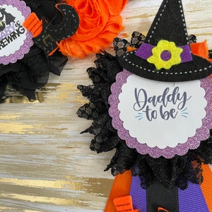 Puede incluir: Favor de fiesta de Halloween con un sombrero de bruja negro, cinta morada y negra y un c&iacute;rculo de purpurina morado con el texto "Daddy to be".