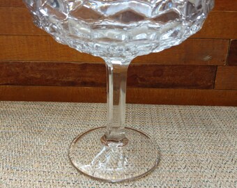May include: A clear glass pedestal bowl with a scalloped edge and a textured design. The bowl is on a tall, slender stem with a wide base.