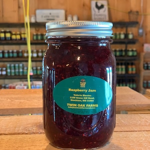 May include: A glass jar of raspberry jam with a green label that reads "Raspberry Jam" and "Twin Oak Farms".