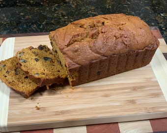 May include: A loaf of pumpkin bread with walnuts and chocolate chips, sliced on a wooden cutting board.