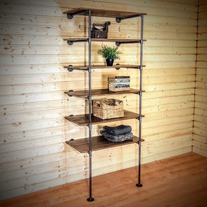 May include: A six-shelf industrial pipe shelving unit with wooden shelves. The shelves are filled with various items, including books, a plant, a woven basket, and folded clothing.