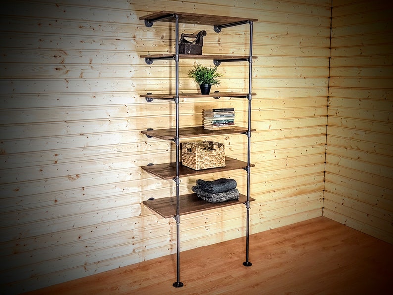 May include: A six-shelf industrial pipe shelving unit with wooden shelves. The shelves are filled with various items, including books, a plant, a woven basket, and folded clothing.