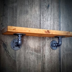 May include: A wooden shelf with black metal pipe brackets. The shelf is mounted on a wood wall.