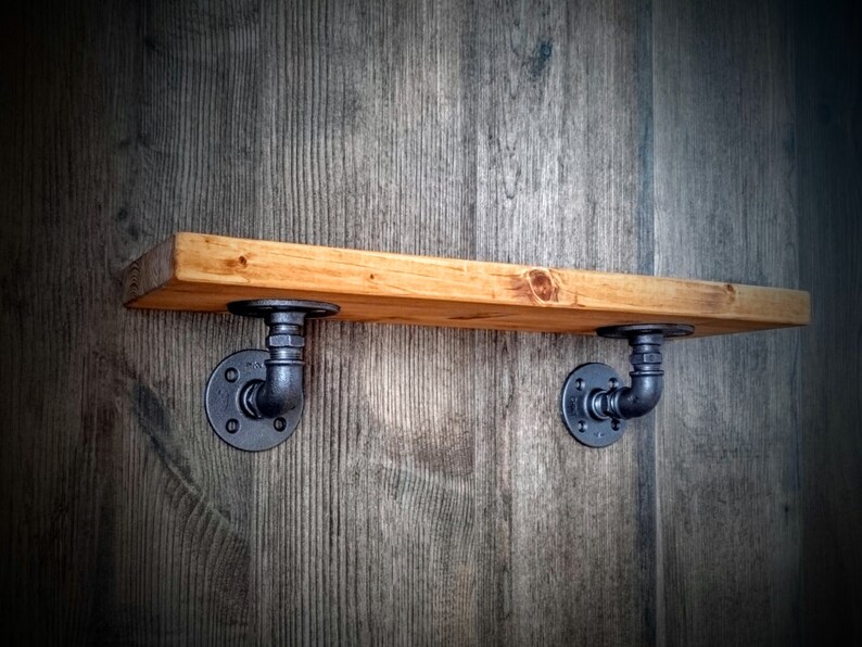 May include: A wooden shelf with black metal pipe brackets. The shelf is mounted on a wood wall.