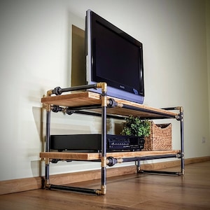 May include: A black metal TV stand with two wooden shelves. The stand has gold accents and is holding a flat screen TV, a black DVD player, and a wicker basket.