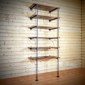 May include: A black metal pipe shelving unit with five wooden shelves. The shelves are made of reclaimed wood and have a rustic look. The unit is mounted to a wall and has a minimalist design.